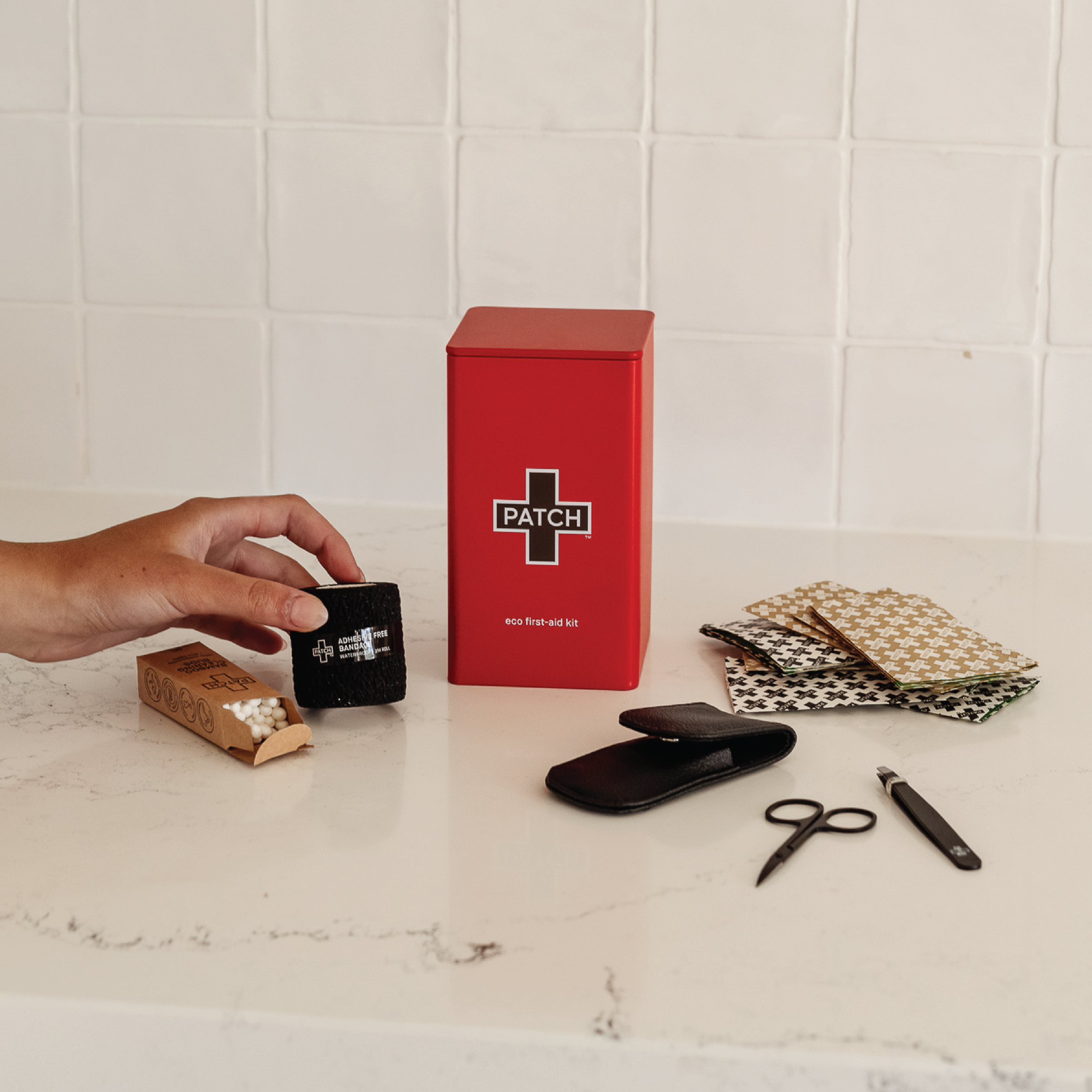 Red 'PATCH' box on a white surface with a hand holding a card, surrounded by various items.