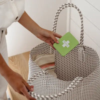 Person holding a woven basket with a green card featuring a white symbol.