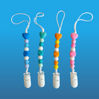 Four colorful pacifier clips with heart-shaped ends on a blue background