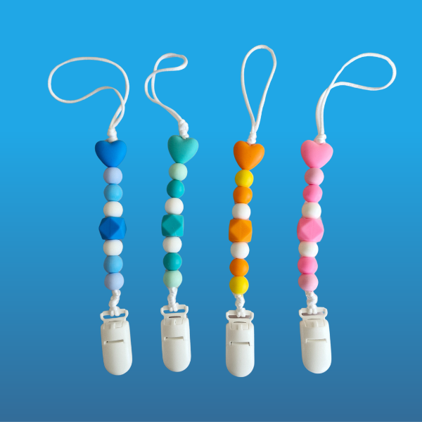 Four colorful pacifier clips with heart-shaped ends on a blue background