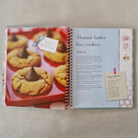 Open cookbook showing a recipe for peanut butter kiss cookies on a textured surface.
