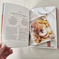 Open cookbook showing a recipe with sliced roasted meat and vegetables on a plate.