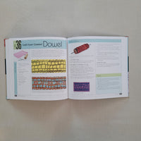 Open book with textile design illustrations using dowel on a plain background