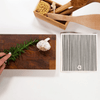Wooden cutting board with herbs and garlic, wooden spoons, and a box of kitchen utensils on a white surface.