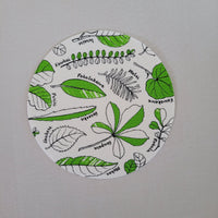 Circular white dishcloth with green and black leaf patterns on a gray background