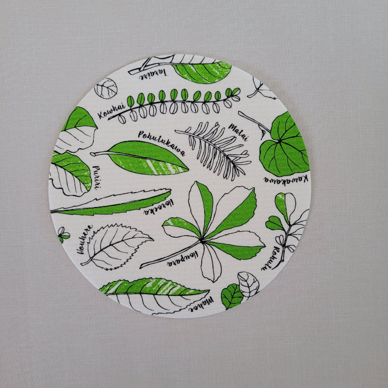 Circular white dishcloth with green and black leaf patterns on a gray background