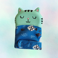 A silicone teething mitt designed to resemble a cat, with a blue patterned sleeve and a white silicone top.