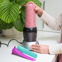 Person holding a pink smoothie in a NutriBullet blender with colorful cups on a white surface.
