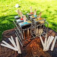 Metallic popsicle mold with popsicle sticks on a wooden surface and grass background