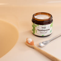 Jar of solid toothpaste with a toothbrush and spoon on a beige background