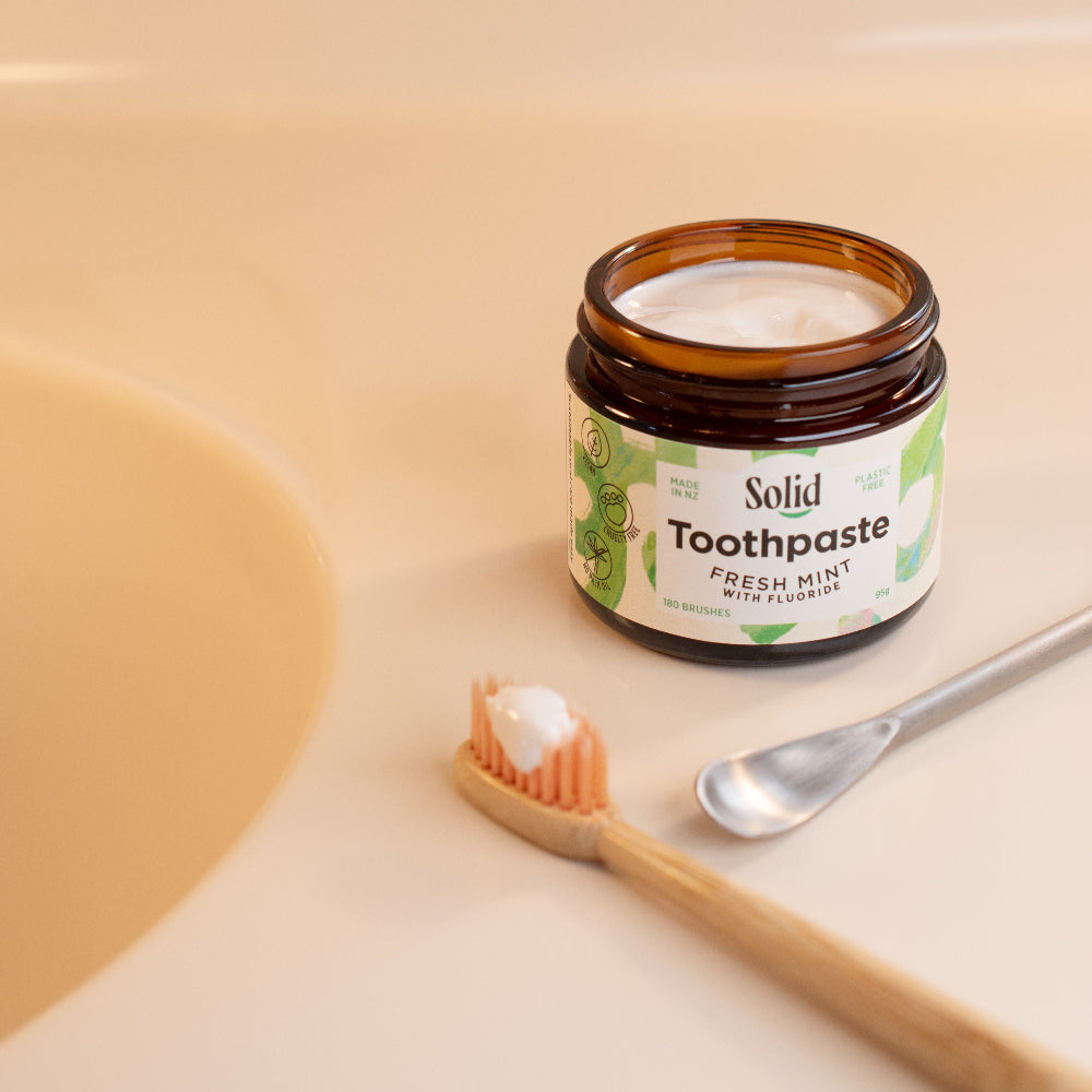Jar of solid toothpaste with a toothbrush and spoon on a beige background