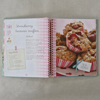 Cookbook with strawberry banana muffin recipe on a textured surface