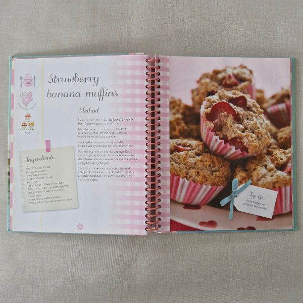 Cookbook with strawberry banana muffin recipe on a textured surface