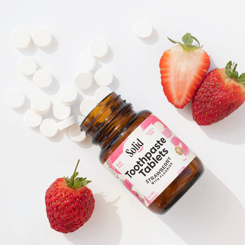 Bottle of Solid Toothpaste Tablets with strawberries on a white background