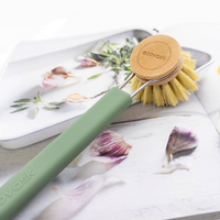 Dish brush with wooden brush head and sage green silicone handle on a floral-patterned surface