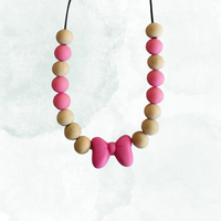 Teething necklace with pink and beige beads and a bow shape pendant on a white background