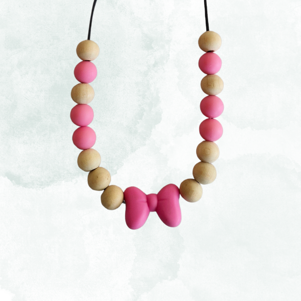 Teething necklace with pink and beige beads and a bow shape pendant on a white background