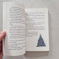 Open book with a Christmas tree illustration on a grey fabric background