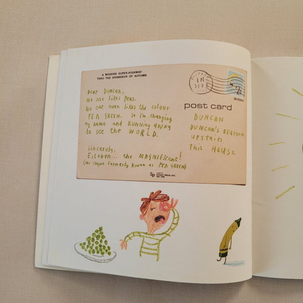 An open book or notebook showing a vintage-style postcard page with illustrated drawings and handwritten text on cream paper, photographed on a beige fabric surface.