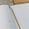 Open notebook with 'Weekly Reflections' section on a wooden surface