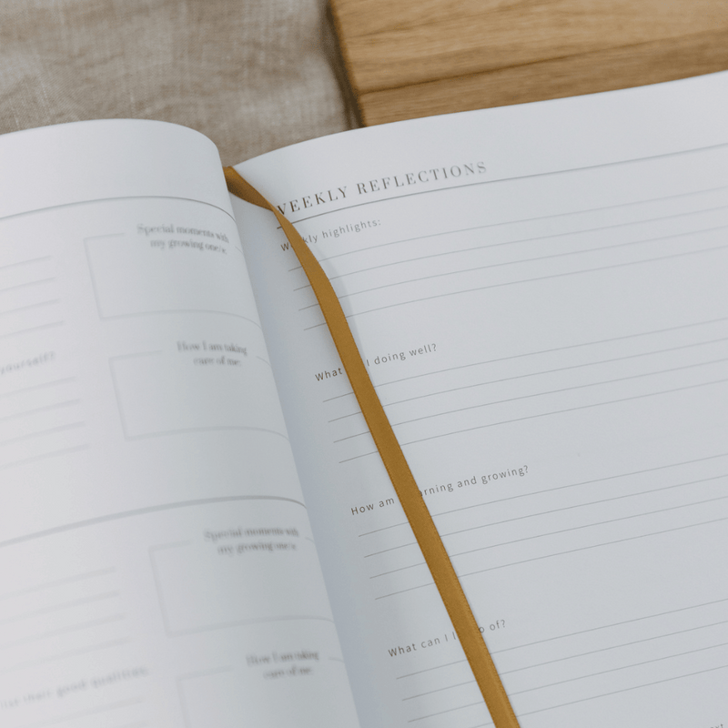 Open notebook with 'Weekly Reflections' section on a wooden surface