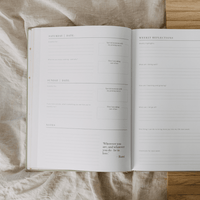 Open planner with daily reflections and notes on a textured fabric surface