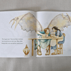 Illustrated book open to two pages with angelic figures and text on a textured fabric background