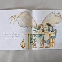 Illustrated book open to two pages with angelic figures and text on a textured fabric background