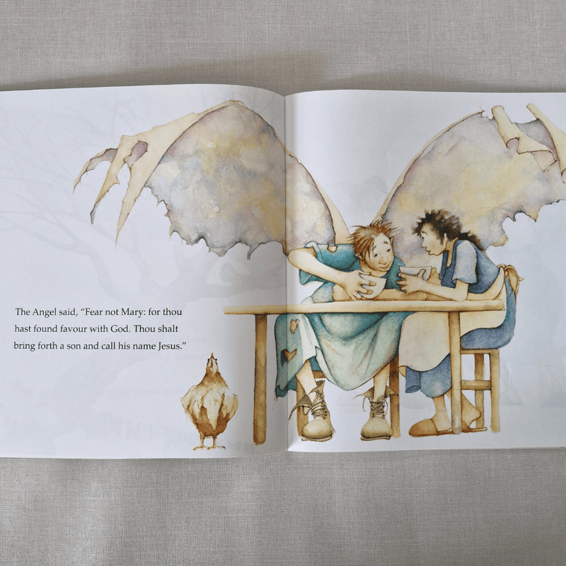Illustrated book open to two pages with angelic figures and text on a textured fabric background