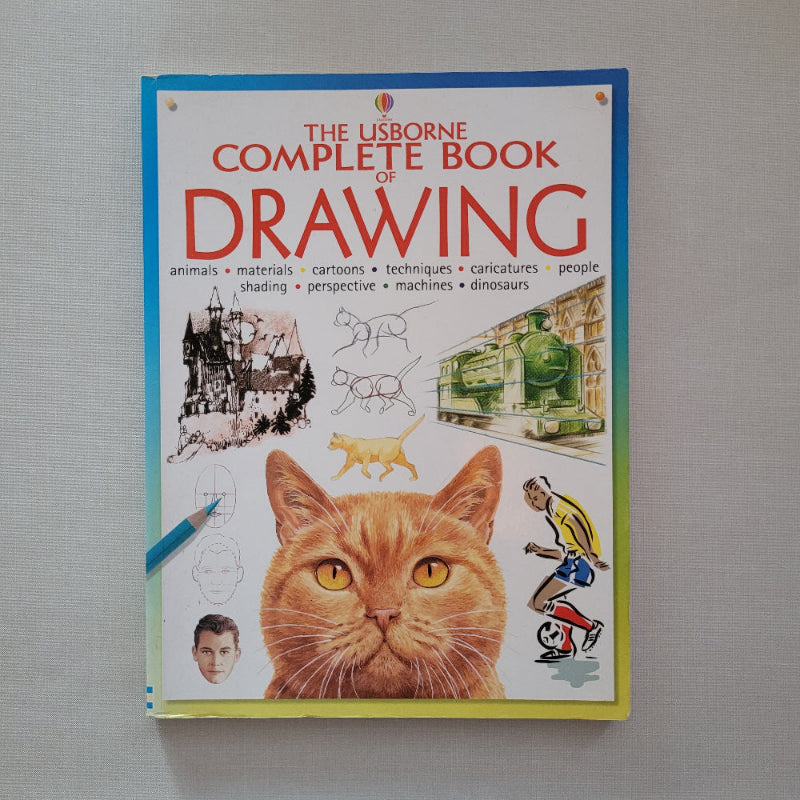 Book titled 'The Usborne Complete Book of Drawing' with a cat illustration on the cover, placed on a gray surface.