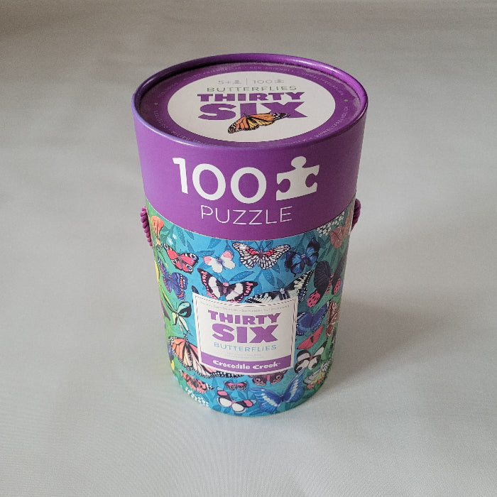 Jigsaw puzzle packaging with a purple lid and colourful body on a white background