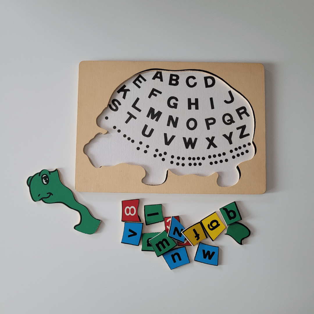 Wooden puzzle with turtle shape and alphabet letters, accompanied by a colourful letter tiles on a light grey background.