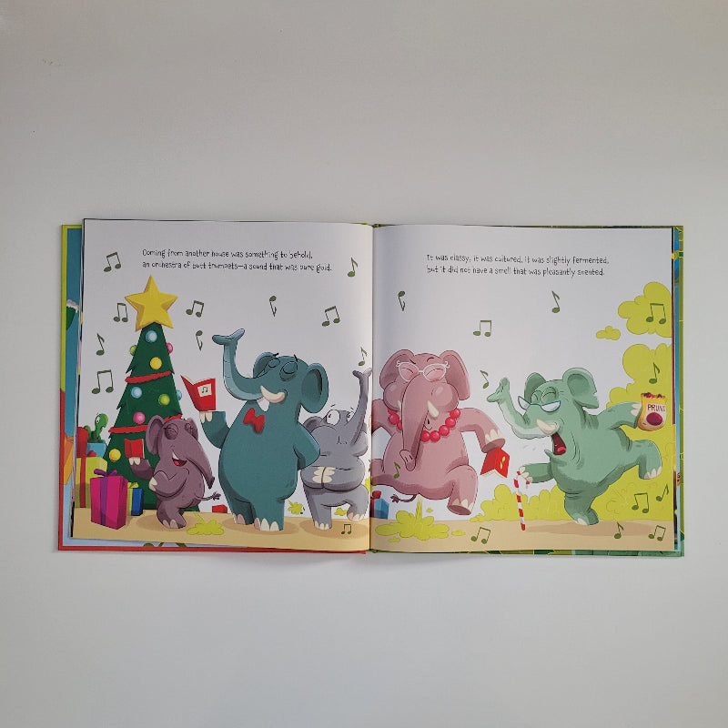An open children's picture book showing two illustrated spread pages with cartoon elephants dancing and celebrating around a Christmas tree, photographed against a plain light background.