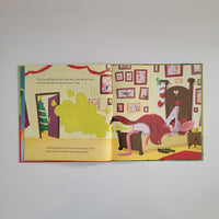 An open children's picture book spread showing a cartoon animal character in bed with a green cloud graphic on the left page and a Christmas stocking on the right page, photographed against a plain light background.