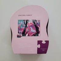 A pink jigsaw puzzle box for the 'Unicorn Forest' puzzle, featuring a colorful illustration of a unicorn and forest on the front, photographed from above on a neutral light gray background.