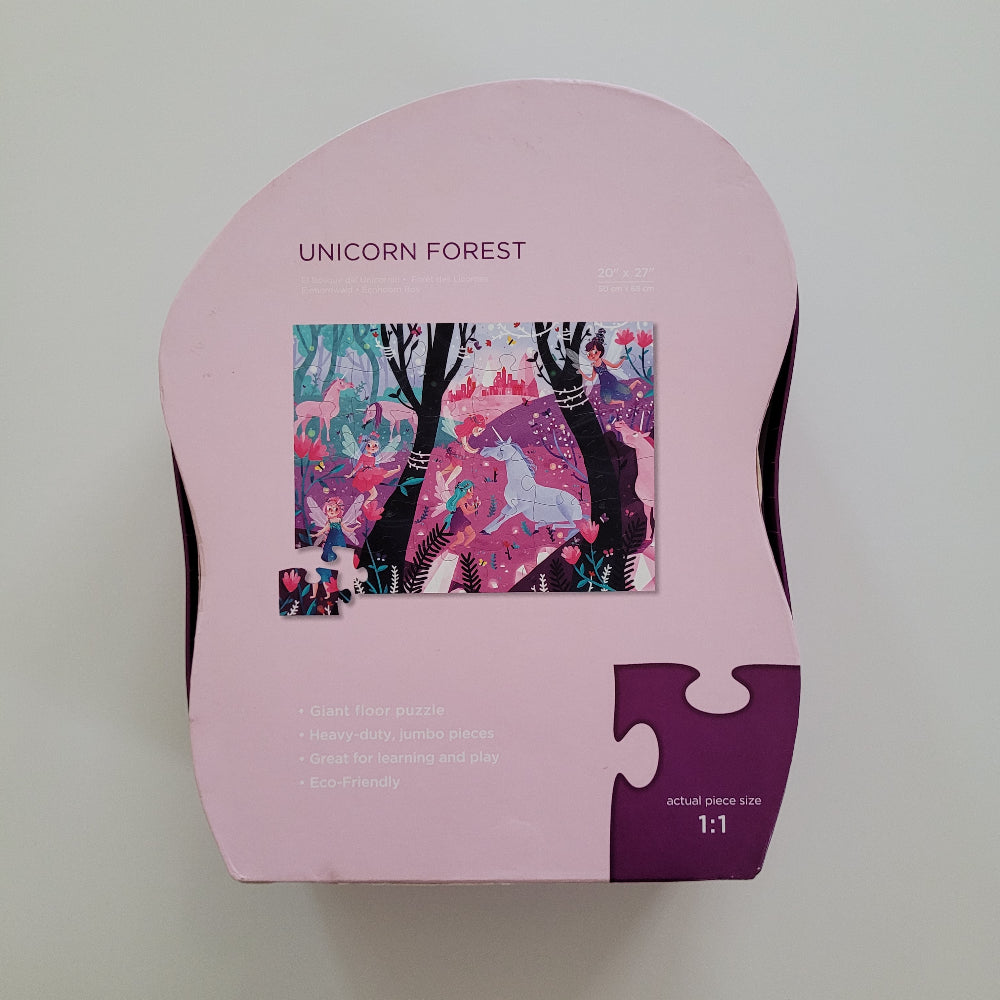 A pink jigsaw puzzle box for the 'Unicorn Forest' puzzle, featuring a colorful illustration of a unicorn and forest on the front, photographed from above on a neutral light gray background.