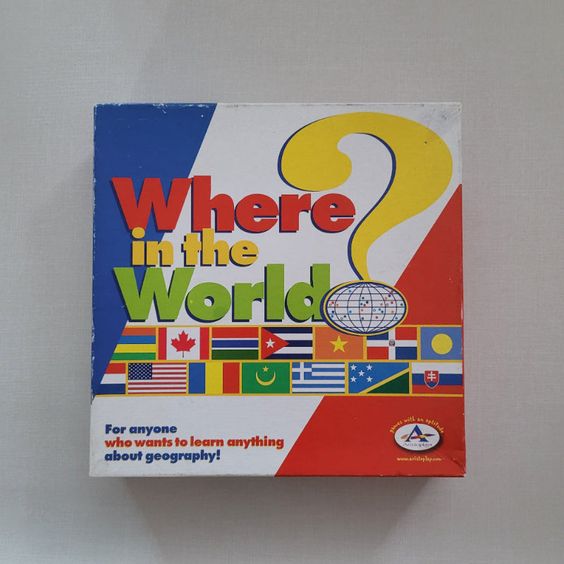 A boxed educational product titled "Where in the World" with a colorful cover featuring a large yellow question mark, red and green title text, a globe icon, and multiple national flags along the right side, photographed on a light gray surface.