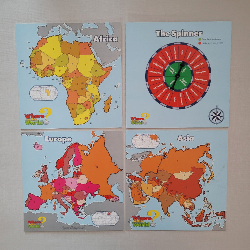 Four educational geography cards for children titled Africa, Europe, Asia, and The Spinner, displayed on a light gray wall. The cards feature colorful, regionally labeled maps and a red-and-green spinner wheel.