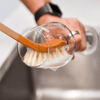 Person cleaning a glass with a wooden scrubber in a kitchen sink.