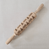 Wooden rolling pin with engraved christmas patterns on a light grey background