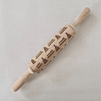 Wooden rolling pin with engraved christmas patterns on a light grey background