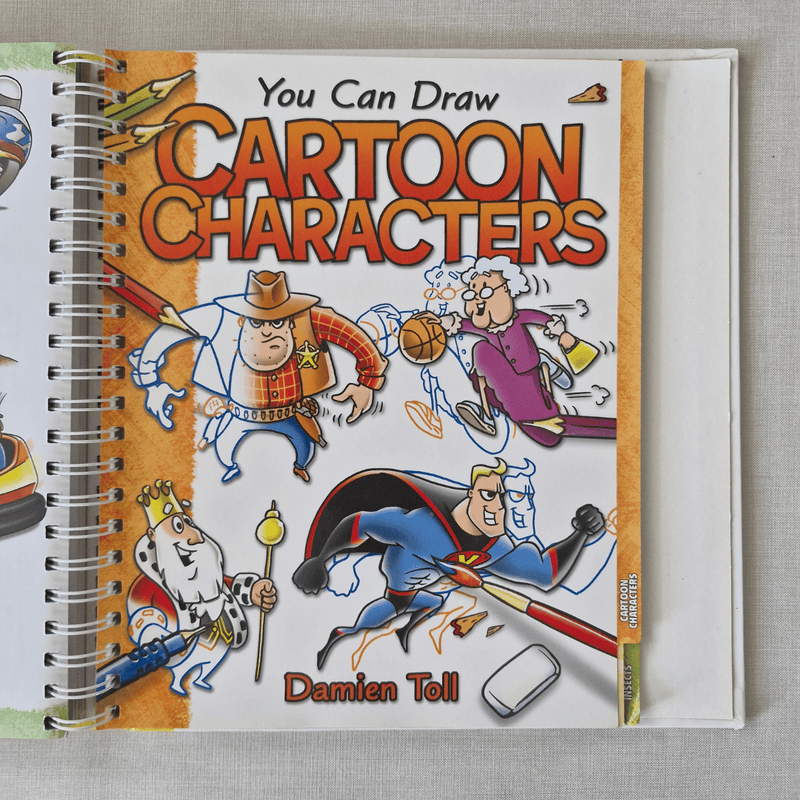 Book titled 'You Can Draw Cartoon Characters' by Damien Toll on a textured surface