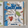 Book titled 'You Can Draw Sea Creatures' by Damien Toll on a textured surface