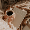 Person holding a cup of coffee next to a book titled 'YOU' on a floral blanket.