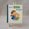 Book titled 'You're a Big Brother' on a stand with a plain background