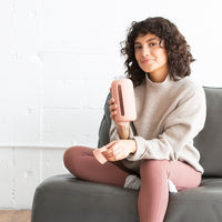 A person sitting on a couch holding a bink glass water bottle with a silicone cover.