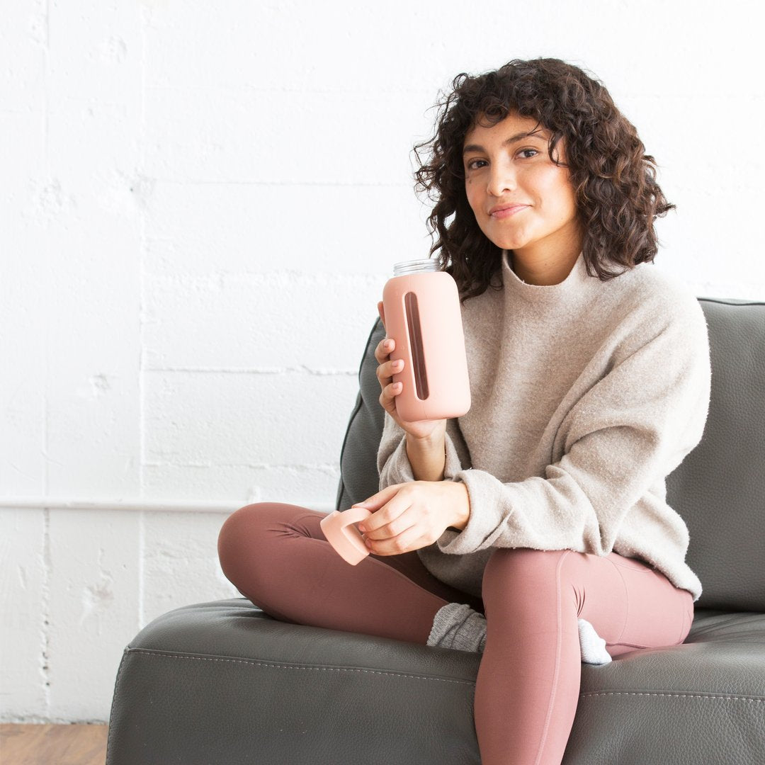 A person sitting on a couch holding a bink glass water bottle with a silicone cover.