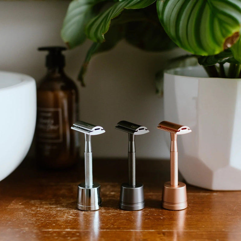 Threerazors on a wooden surface with a bowl and plant in the background
