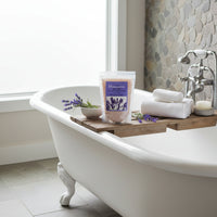 lavender bath salts sitting on an overbath cady, with white claw foot tub