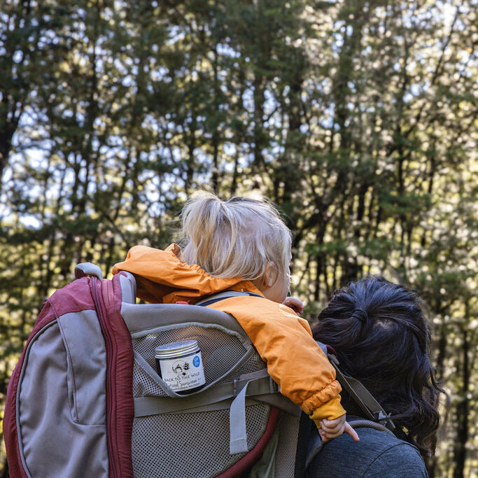Person with a child on their back in a forest with sunscreen in pack